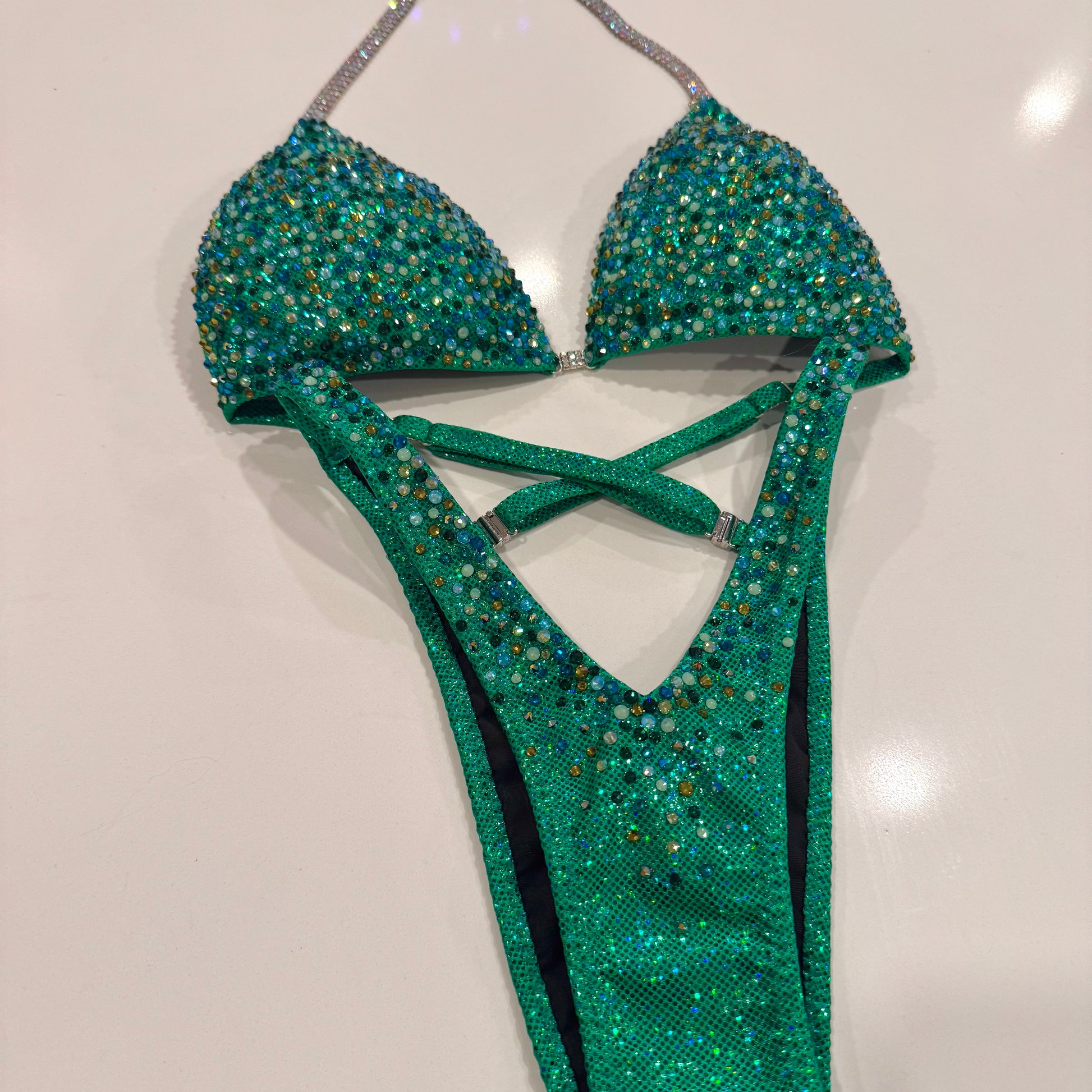 A green glamour suit with a holographic base and multicolored stone embellishments, featuring adjustable straps and silver connectors. Denver, Colorado
