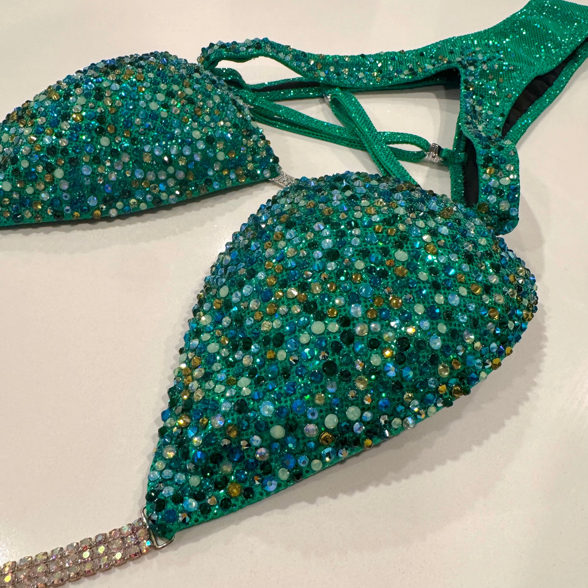 A green figure suit with a holographic base and multicolored stone embellishments, featuring adjustable straps and silver connectors. Denver, Colorado