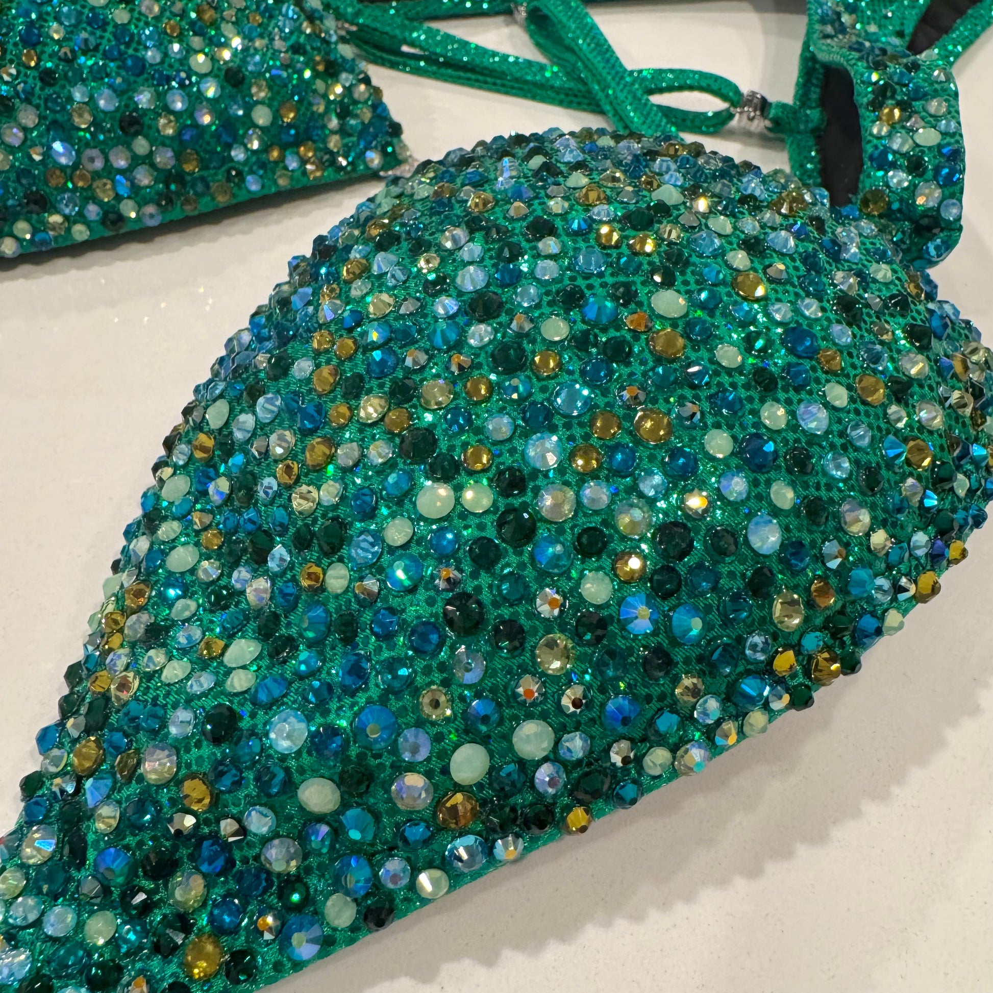 A green figure suit with a holographic base and multicolored stone embellishments, featuring adjustable straps and silver connectors. Denver, Colorado