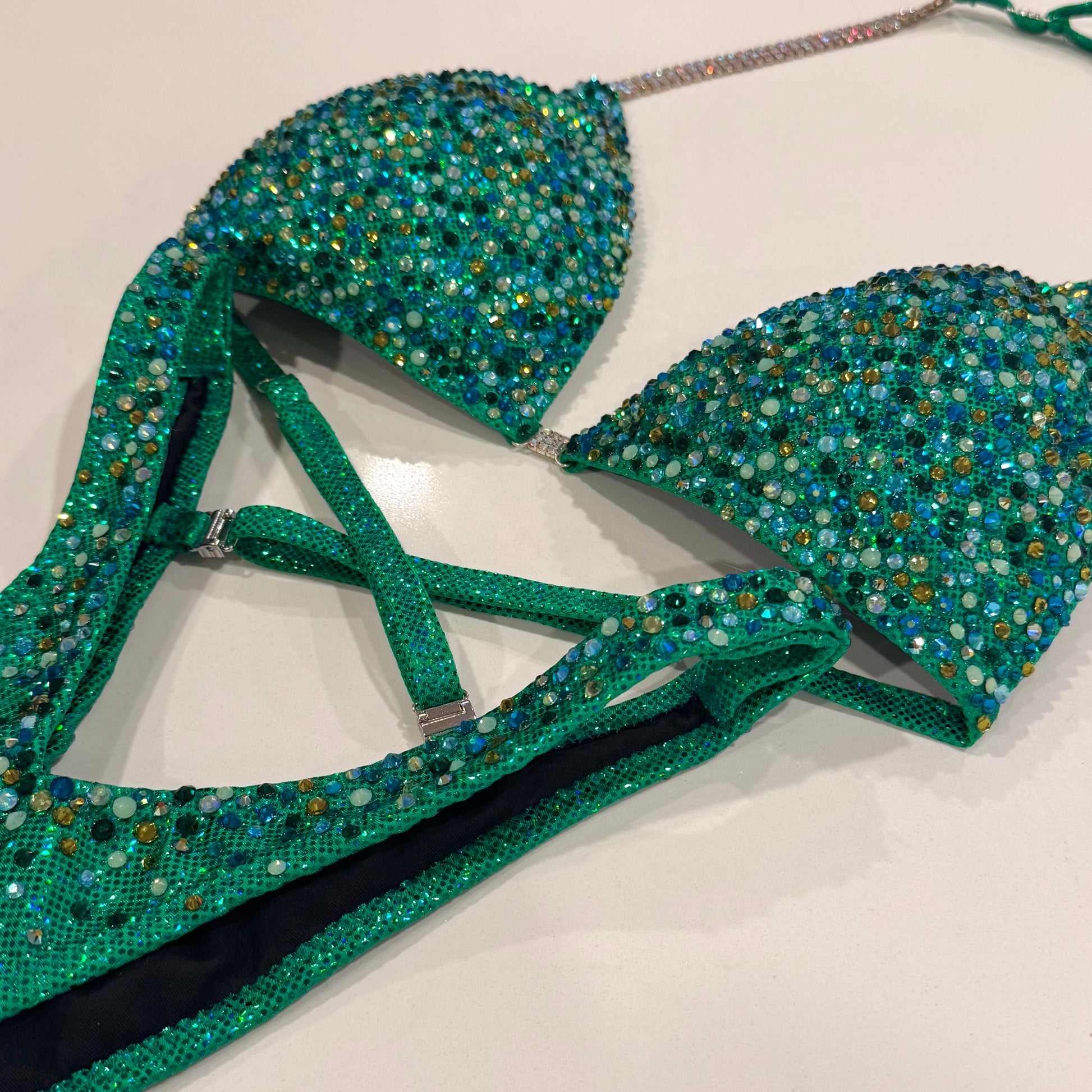 A green figure suit with a holographic base and multicolored stone embellishments, featuring adjustable straps and silver connectors. Denver, Colorado
